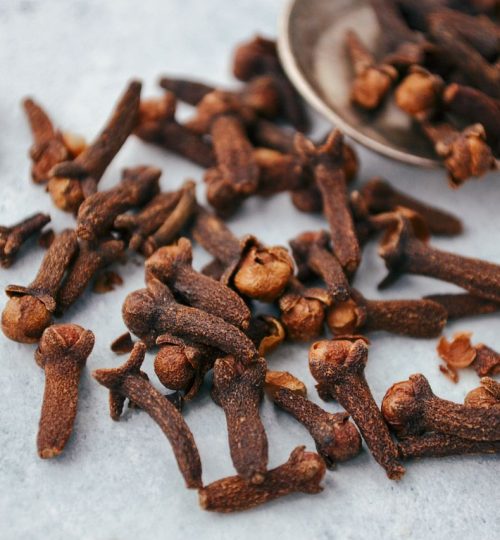 A close-up image of aromatic dry cloves scattered on a spoon over a gray surface.